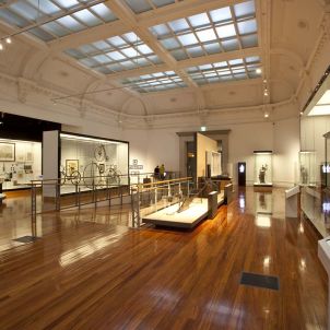 A spacious museum interior featuring wooden floors, display cases with artifacts, and decorative ceilings.